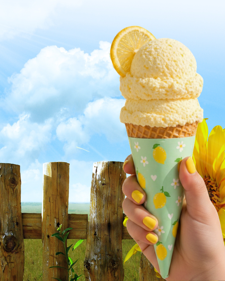 Hand holding a lemon ice cream cone with a printable lemon cone wrapper against a sunny rustic outdoor background with sunflowers and blue sky.